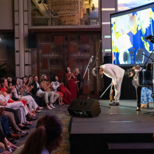 Violinist and pianist taking a bow to enthusiastic applause, a colourful artwork projected behind them