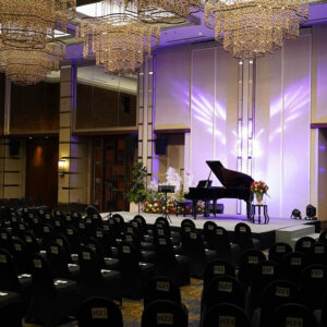 Grand piano on stage flanked by floral arrangements and purple lighting in the empty resort ballroom