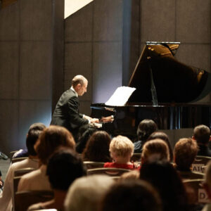 Pianist performing at a grand piano lit by a soft spotlight as a captivated audience looks on up close